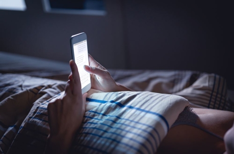 Woman laying in bed texting on phone